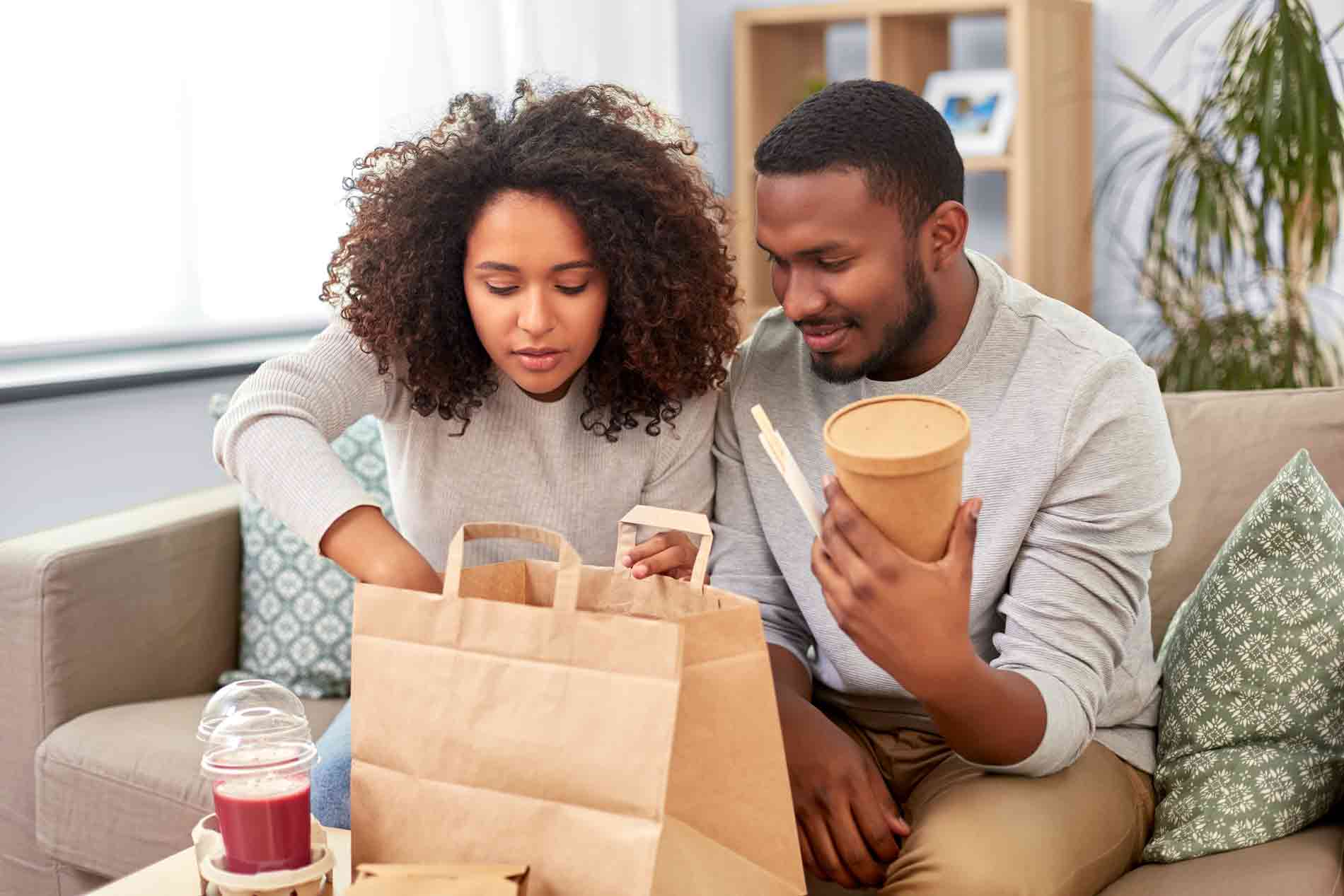 A man and woman take their delivery food out of the paper bag at home.