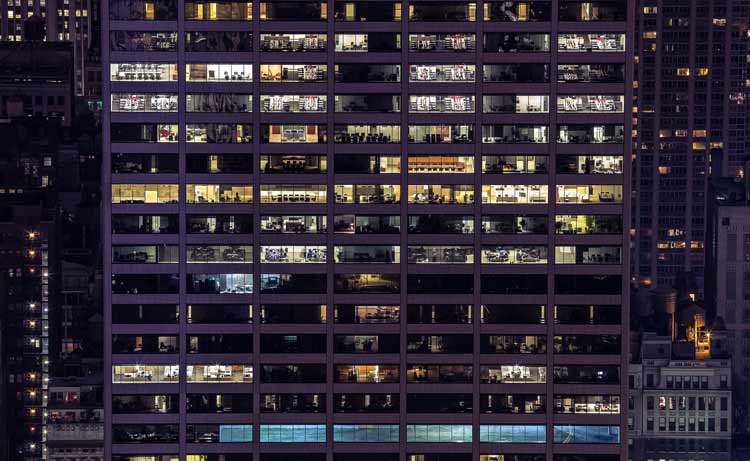 Rooms are lit inside a large glass office building on a city night